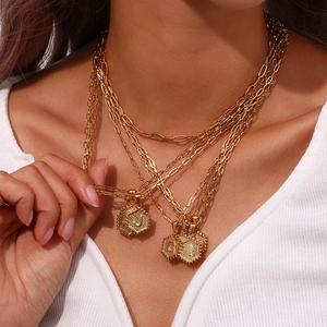 Detail of layered gold hexagon initial necklaces J, G, L on model with white shirt