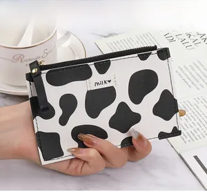 Close-up of slim cow print coin purse with milk logo held over a marble table