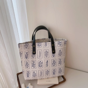Detail of canvas tote bag featuring blue floral pattern and black leather handles