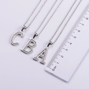 Size comparison of silver A, B, and C letter necklaces with rhinestones beside a ruler