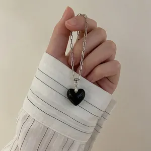 Detail of silver paperclip chain necklace with a black heart pendant held by hand
