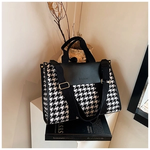 Detail of vintage houndstooth tote bag with black leather flap on a book backdrop