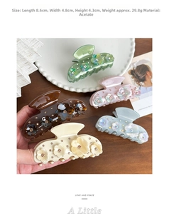 Detail view of five acetate flower hair claws with rhinestone accents in soft pastel colors