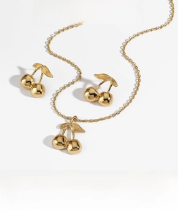 Detail of gold cherry necklace and earrings set with PVD plating on white background