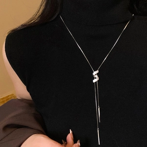 Dettaglio della collana con ciondolo a S in zirconi e nappa lunga su un maglione nero