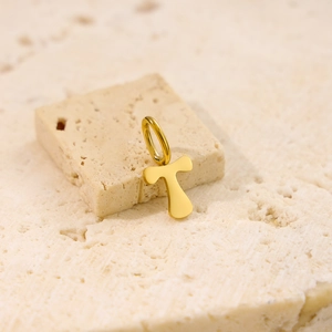 Macro shot of gold letter T pendant on a textured beige stone base with polished finish