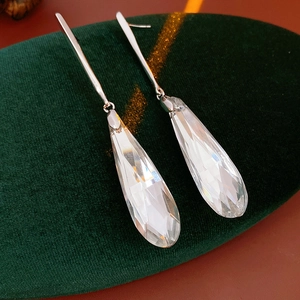 Detailed view of silver needle glass teardrop earrings on a luxury green velvet cushion