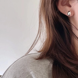 Macro side view of a minimalist silver teardrop earring worn on a female ear model