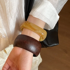 Close-up of geometric resin bangles in amber and dark brown worn with a chic outfit