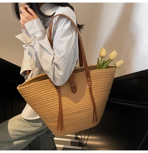 Detail of woven beach tote bag with leather straps and elegant tassel on model
