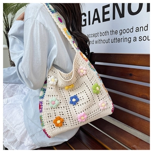 Detail of woven beach bag featuring colorful crochet flowers and wide shoulder strap