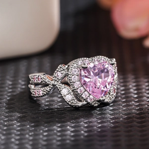 Macro shot of silver ring with pink heart-shaped gemstone and crystal bow design