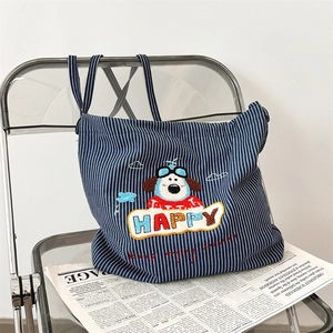 Detail of cute puppy embroidery on a blue striped canvas tote bag over newspapers