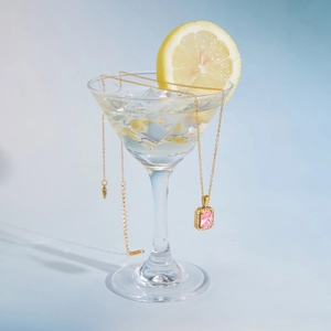 Detail of pink zircon pendant on gold necklace draped over a cocktail glass with ice