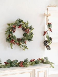 Detailed Christmas garland with pine cones, red berries, and gold bells on a white wall