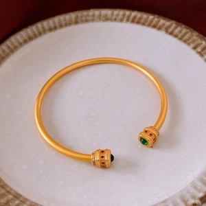 Gros plan d'un bracelet doré 18 carats avec pierres vertes et détails en émail rouge
