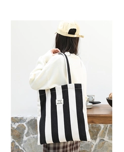 Detail of a large black and white striped canvas tote bag worn by a model in casual style