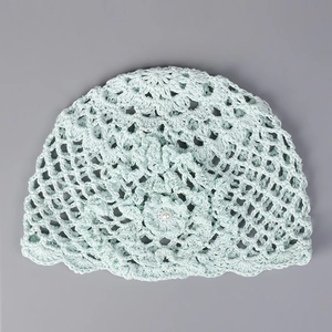 Détail du chapeau au crochet vert menthe avec maille ajourée, fleur en perle et bord ondulé