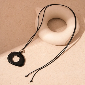 Detail of vintage black resin oval pendant with cord necklace on a textured stone surface