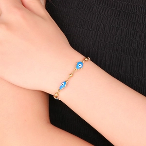 Detail of gold-plated Hamsa Hand bracelet featuring blue evil eye charms on a model