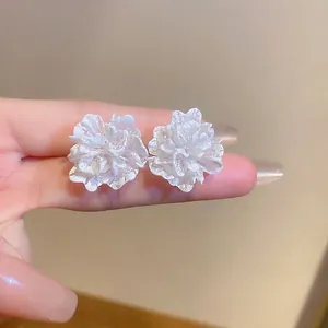 Macro shot of 3D white flower stud earrings with layered petal textures and matte finish