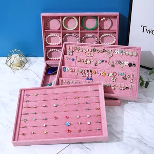 Stack of pink velvet jewelry display trays for rings and earrings on marble surface