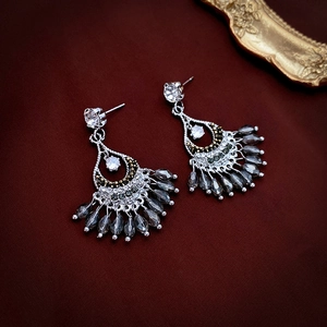 Detail of fan-shaped ethnic earrings with grey crystals on red textured fabric