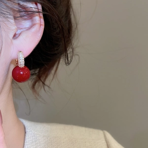 Close-up of red zircon resin hoop earring with gold diamond-encrusted accents on ear