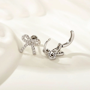 Minimalist silver bow earrings with zircon stones on soft cream fabric background