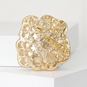 Exquisite gold hollow flower brooch with rhinestone accents on a minimalist background