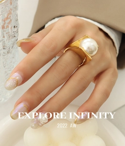 Detail shot of a geometric gold ring featuring a large white faux pearl on a square setting