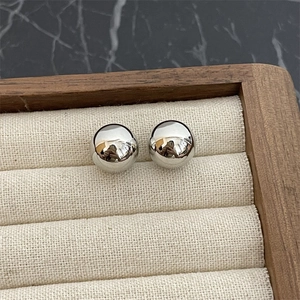 Detailed view of polished silver spherical stud earrings on a linen jewelry display tray
