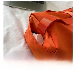 Detail view of the orange oxford fabric crossbody bag showing the functional side pocket