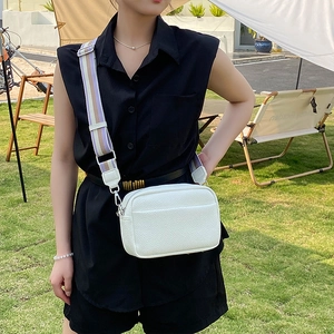 Outdoor view of white crossbody bag with purple striped wide strap on grass lawn