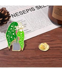 Detailed macro view of an enamel green plant brooch with metallic backing on wood surface