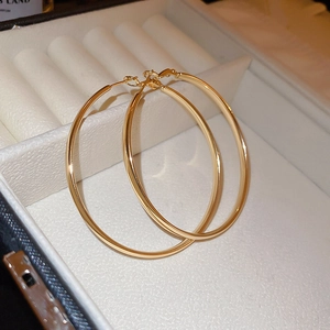Detailed view of polished large golden hoop earrings in a white textured jewelry box