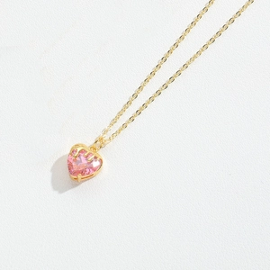 Macro detail of a heart-shaped pink zircon pendant on a delicate gold chain necklace