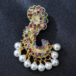 Macro detail of luxury gold C-shape brooch with colorful rhinestones and hanging pearls