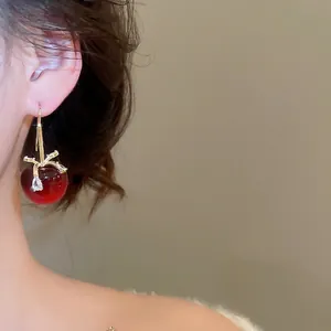 Eleganti orecchini a ciliegia in resina rossa con accenti dorati su una modella