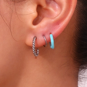 Detailed view of silver twisted hoop earrings and blue enamel ring on ear