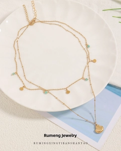 Detail of a layered gold titanium necklace with fan pendants on a white ceramic plate