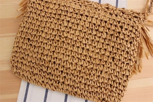 Close-up of handmade straw woven bag with fringe detail on a rustic wooden table