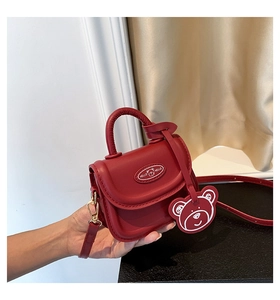 Detail of red mini crossbody bag featuring a cartoon bear charm and Hello tag decoration