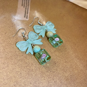 Detail of sweet bow-shaped earrings with light green resin and floral transparent drop