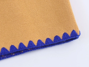 Detailed close-up of yellow knit cardigan with contrasting bright blue scalloped crochet edge