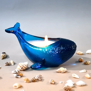 Close-up of a lit candle inside a whale-shaped blue glass mold with ocean seashell decor