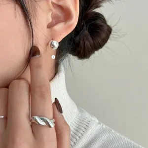 Detail of twisted 925 sterling silver ring and ball studs on model wearing white sweater