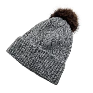 Detailansicht der Textur einer grauen Strickmütze mit flauschigem dunklem Pelzbommel