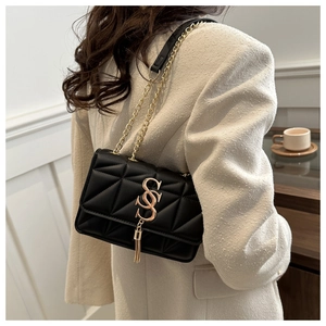 Detail showing a black quilted chain bag with a gold S-logo and fringe tassel decoration
