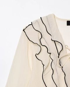 Dettaglio di elegante camicetta con scollo a V, balze a strati e raffinati bordi neri